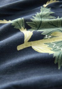 Textilie s tmavě modrou backgroundem a vzorem rostlin v zelené a žluté barvě. Tkanina má jemnou strukturu s hladkými sklady.