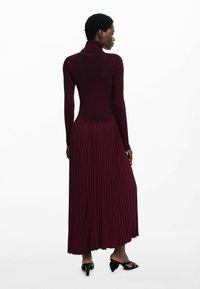 Bordeaux ribbet turtleneck kjole med plisseret nederdel, der har en tætsiddende overdel og en flydende bund. Glat tekstur, ankel-længde design.