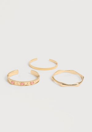 Tre braccialetti aperti color oro; uno con pietre rosa e bordi testurizzati, uno con scanalature verticali e uno con forma esagonale irregolare.