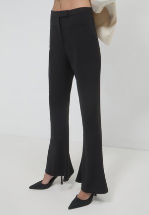 Schwarze, weit geschnittene Hosen aus glattem Stoff, mit Seitentaschen und tailliertem Schnitt, kombiniert mit schwarzen, spitzen High Heels.