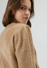 Lichtbruine, gemêleerde trui met een ronde hals en afgezakte schouders, met een zachte textuur en subtiele stikdetails.