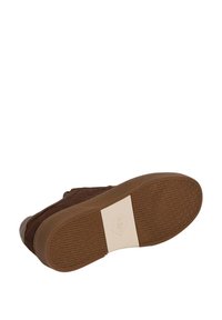 Zapatillas de ante marrón con suela de goma. Presentan un patrón de agarre texturizado, una etiqueta blanca contrastante en la entresuela y un diseño de puntera redondeada.