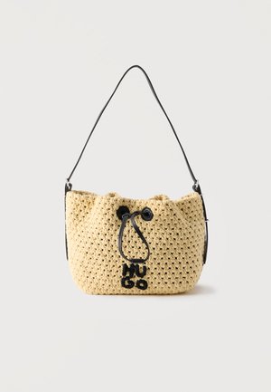 Beige crocheted bucket bag with black drawstring closure and black shoulder strap, featuring a small black stitched logo on front.