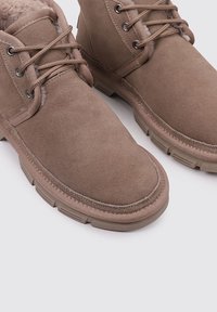 Beige Wildleder-Stiefeletten mit einem weichen Innenfutter. Features: runde Zehenform, Metallösen und Schnürverschluss. Die dicke Gummisohle sorgt für guten Halt.