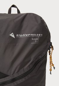 Schwarzer Rucksack mit strukturierten Oberflächen, hervorgehobenen Reißverschluss, bunten Zugkordeln und weißem Druckbranding. Kompaktes Design, 5L Fassungsvermögen.