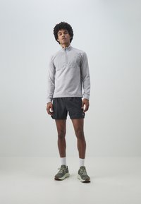 Ljusgrå långärmad pullover med halvdragkedja, svarta shorts och grå sportskor. Har strukturerad tyg och enkel design.