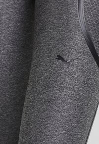Szare legginsy sportowe wykonane z teksturowanej tkaniny, z czarnym logo Pumy i kontrastującym czarnym paskiem wzdłuż boku.