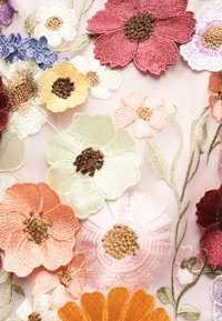 Χρωματιστά κεντητά λουλούδια με λεπτομερή πέταλα και κέντρα σε διαφανές ροζ ύφασμα, που δείχνουν πράσινα κεντητά φύλλα και στελέχη.