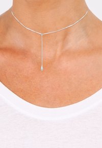 Collier ras du cou en argent avec une chaîne délicate et un pendentif en forme de goutte suspendu au centre. Texture lisse avec un design minimaliste.