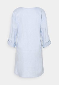 Tunique en lin bleu clair avec un col rond, manches trois-quarts retroussées aux poignets, et une coupe ample. Design minimaliste, sans motifs.
