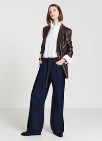 Blazer en cuir marron, chemise à rayures blanches et pantalon en denim foncé à pattes larges avec une taille à nouer. Textures lisses et détails de design sur mesure.