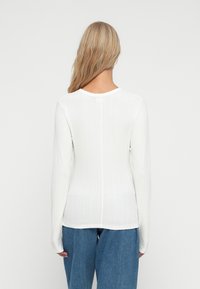 Langærmet, ribbet hvid top med rund halsudskæring og en midtersøm, parret med løse, lyseblå jeans. Glat tekstur, tætsiddende design.