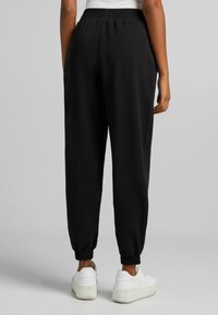 Svarta sweatpants med en samlad elastisk midjeband och smalnande mudd, tillverkade av ett mjukt material, i kombination med vita sneakers.