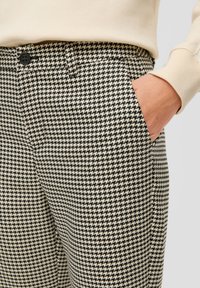 Pantalons à motif pied-de-poule noir et beige avec une texture lisse ; dotés d'une poche latérale et d'une fermeture à bouton à la taille.