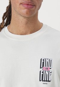Weißes Baumwoll-T-Shirt mit rundem Halsausschnitt, das auf der Vorderseite einen grafischen Druck in Schwarz, Rosa und weißem Text mit der Aufschrift "FIND ALLA FINE JUVENTUS" zeigt.