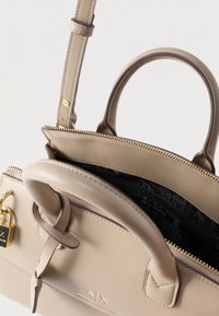 Μπεζ δερμάτινη τσάντα Armani Exchange με χρυστό φερμουάρ, χερούλια, χρυσό κλείδωμα και εσωτερική επένδυση με λογότυπο.