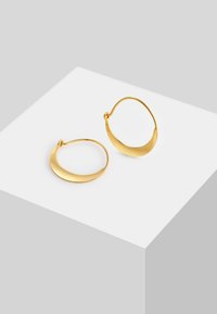 Pendientes de aro de metal dorado con un diseño suave y curvado. Con apertura dividida para facilitar el uso, presentan un acabado pulido.
