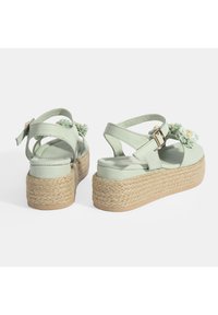 Minzgrüne Plateausandalen mit überkreuztem Riemen-Design, aus Kunstleder, floralem Schmuck, jutegewebter Sohle und Schnallenverschluss.
