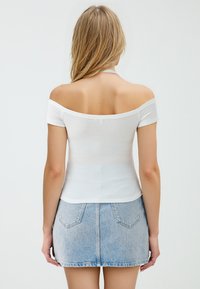 Biała bluzka typu off-the-shoulder z prążkowanego materiału, zestawiona z jasnoniebieską mini spódnicą dżinsową, charakteryzującą się dopasowanym krojem i krótkimi rękawami.