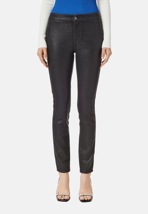 Frau trägt schwarze Slim-Fit-Hose, blau-weißes langärmeliges Oberteil und schwarze offene Absatzschuhe, steht mit entspannten Armen an den Seiten.