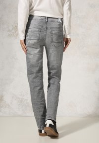 Jean gris avec une finition légèrement délavée, coupe droite, deux poches arrière, et contrasté avec des baskets noires avec des accents blancs.