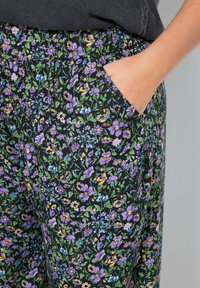 Bloemmotieven broek met een zwarte achtergrond en paarse, blauwe en groene bloemen; bevat een zijzak voor functionaliteit.