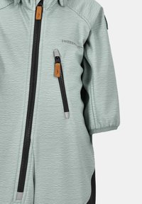 Ljusgrön zip-up jacka med ett strukturerat vågmönster, svarta detaljer, framzipper och läderdragflikar på zippen.