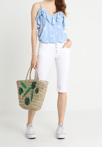 Vaaleansininen, röyhelöinen hihaton paita, jossa on valkoinen kukkakuvio, yhdistettynä valkoisiin capri-housuihin ja kudottuun olkikassiin, jossa on vihreitä ja vaaleanpunaisia yksityiskohtia.