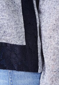 Graues Strickoberteil mit einem marineblauen Spitzeneinsatz an einer Seite, mit strukturierter Oberfläche. Kombiniert mit hellblauem Denim.