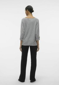 Grå strikbluse med vid halsudskæring, trekvartærmer oprullet, parret med sorte, lige ben bukser. Minimalistisk design og letvægtsstof.