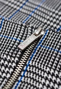 Tissu pied-de-coq noir et blanc avec des accents bleus, doté d'une fermeture éclair argentée avec "Superdry" gravé sur la tirette.