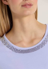 Lichtpaarse top met een ronde halslijn, versierd met een band van kleine sprankelende kralen langs de kraag, gladde stoftextuur.