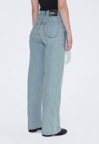 Vaqueros de pierna ancha de tiro alto en azul claro con un acabado desvanecido, que cuentan con bolsillos traseros y una etiqueta de marca negra en la cinturilla.