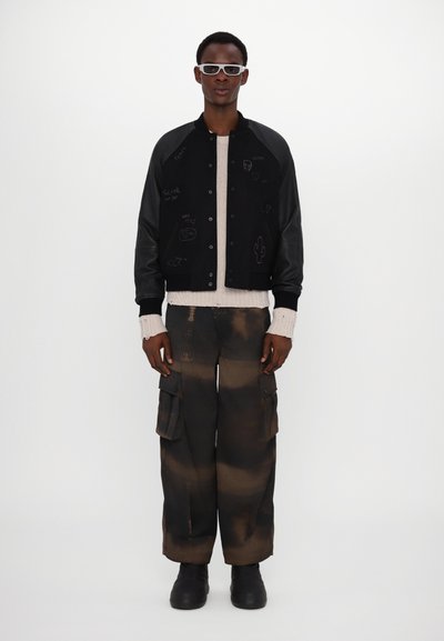 Blouson en cuir noir avec des manches en cuir, motifs brodés, un pull crème et un pantalon cargo oversize marron avec un motif délavé et des poches.