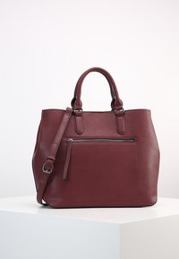 Bordeaux leren handtas met dubbele handvatten aan de bovenkant, afneembare schouderriem, ritsvak aan de voorkant en een gladde textuur.