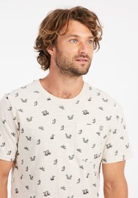 Camiseta de manga corta color crema con un estampado multicolor de temática playera. Cuenta con un bolsillo en el pecho y un escote redondo. La textura de la tela parece suave.