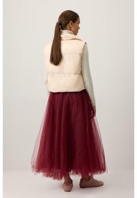 Világos rózsaszín puffos mellény egy szürke pulóver fölött, bordó tüll szoknyával és puha rózsaszín cipővel párosítva. Sima textúra, réteges kialakítással.