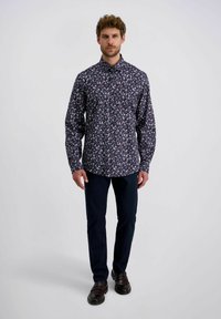 Navy bloempatronde shirt met een button-down kraag, lange mouwen en een ontspannen pasvorm, gecombineerd met donkere broek en bruine schoenen.