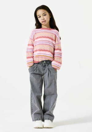 Gebreide trui met roze, witte en gele strepen, gecombineerd met hooggesneden grijze denim broek. Model draagt witte sneakers. Eenvoudige achtergrond.