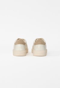 Baskets beiges avec une tige synthétique texturée de couleur claire. Accents en suède doux au niveau du talon. Semelle en caoutchouc avec le nom de la marque en relief.