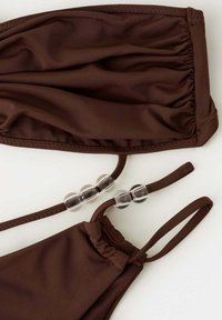 Bikini marron avec haut bandeau froncé et bas triangulaire, tous deux avec de fines bretelles ornées de perles rondes transparentes sur fond blanc.