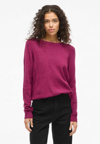 Maglione fucsia in maglia con scollatura a barca e maniche lunghe, caratterizzato da polsini a coste e una vestibilità rilassata, indossato con pantaloni neri.