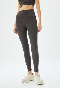 Czarne legginsy sportowe z wysokim stanem, wykonane z elastycznego materiału, z bezszwowym wzornictwem i dopasowanym krojem. W zestawie z jasnymi butami sportowymi.