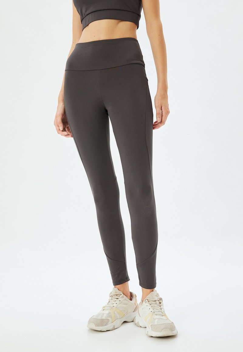 Czarne legginsy sportowe z wysokim stanem, wykonane z elastycznego materiału, z bezszwowym wzornictwem i dopasowanym krojem. W zestawie z jasnymi butami sportowymi.