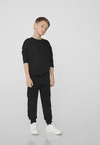 Černá mikina s přední kapsou, spárovaná s černými cargo kalhotami se bočními kapsami a žebrovanými manžetami, doplněná bílými teniskami.