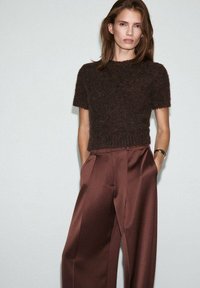 Brauner, flauschiger Kurzarm-Pullover kombiniert mit hoch sitzenden, weiten braunen Satin-Hosen. Einfaches Design mit einer softweichen Textur.