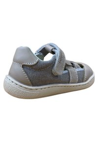 Zapatillas de lona y cuero grises con tira de velcro, que presentan costados abiertos y suela de goma texturizada. Punta y talón reforzados.