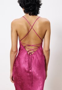 Satijnen fuchsia jurk met gekruiste spaghettibandjes en een lace-up detail op de rug. Gladde textuur met een subtiel bloemenpatroon.