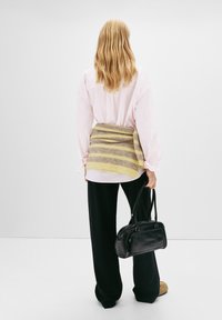 Oversized shirt met roze en witte strepen, gelaagd met een beige en gele gestreepte sjaal, gecombineerd met zwarte wijde broek en een zwarte handtas.
