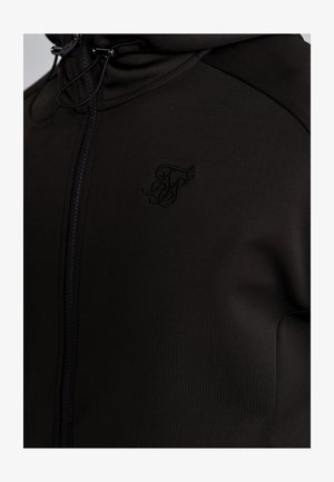Black zip-up jacket made of smooth fabric, featuring a raised logo on the chest, high collar, and adjustable drawstring.
